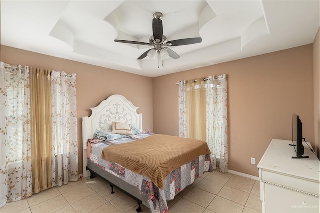 bedroom featuring a tray ceiling, light tile patterned floors, baseboards, and ceiling fan