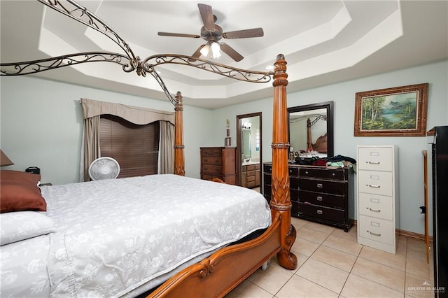 tiled bedroom with ceiling fan, a tray ceiling, and ensuite bath