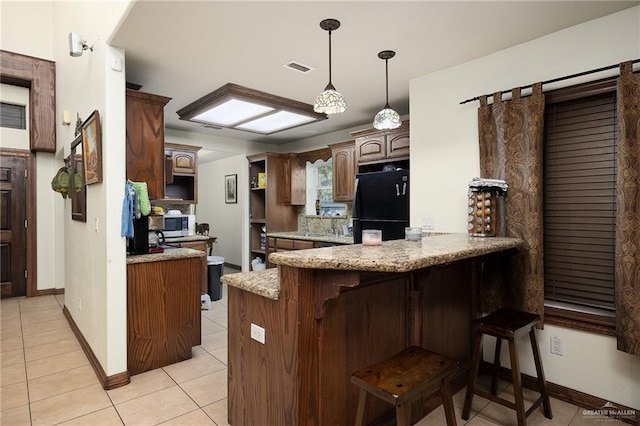 kitchen featuring black refrigerator, light stone counters, kitchen peninsula, and light tile patterned floors