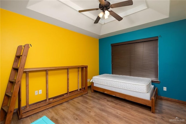 bedroom with hardwood / wood-style floors, a raised ceiling, and ceiling fan