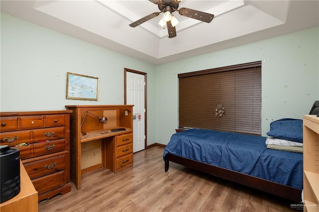 bedroom with light wood-type flooring, a tray ceiling, and ceiling fan