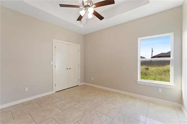 unfurnished room featuring ceiling fan, light tile patterned floors, and a tray ceiling