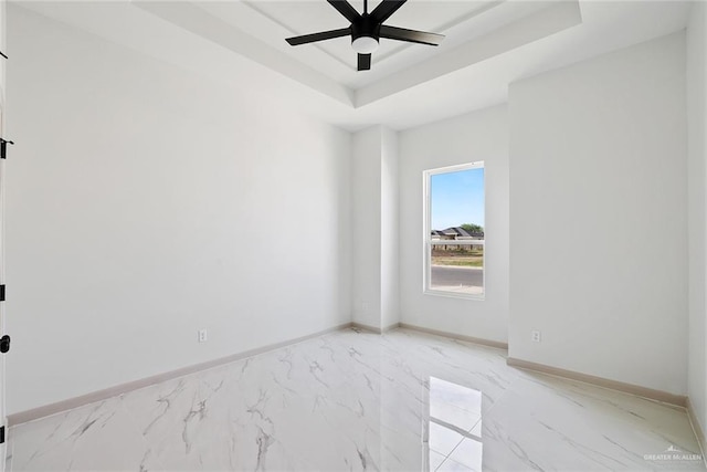 unfurnished room featuring a raised ceiling, a ceiling fan, baseboards, and marble finish floor