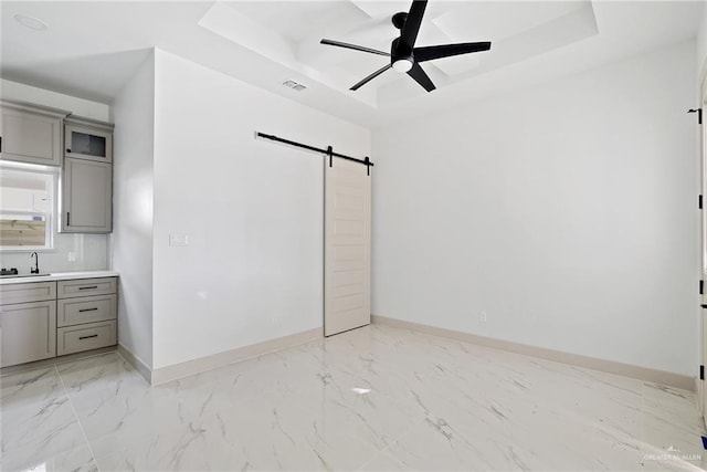 interior space with a sink, a barn door, a raised ceiling, and baseboards