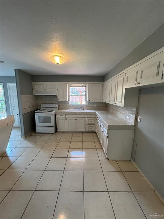 kitchen with backsplash, electric range, white cabinetry, tile counters, and light tile patterned flooring