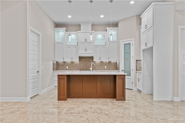 kitchen featuring hanging light fixtures, an island with sink, and white cabinets