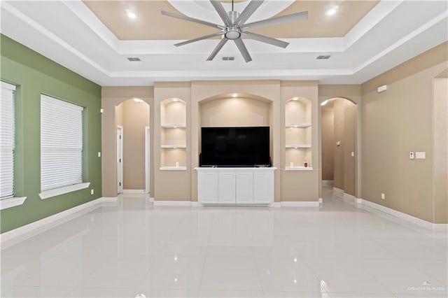 unfurnished living room featuring light tile patterned floors, built in shelves, a raised ceiling, and ceiling fan