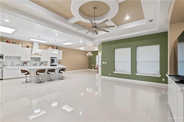 kitchen featuring a kitchen breakfast bar, pendant lighting, ceiling fan with notable chandelier, decorative backsplash, and white cabinets