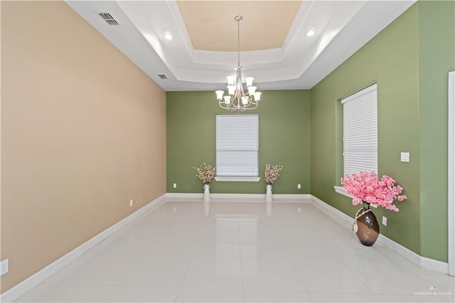 tiled empty room featuring a raised ceiling and a chandelier