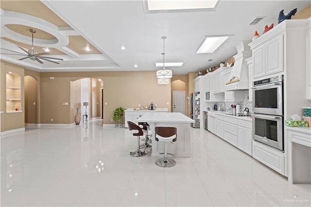 kitchen featuring white cabinetry, stainless steel appliances, a kitchen breakfast bar, a center island, and decorative light fixtures