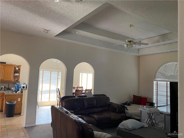 2500 W Xanthisma Ave, Mcallen, TX 78504 - living area featuring a tray ceiling, light tile patterned floors, a ceiling fan, a textured ceiling, and arched walkways