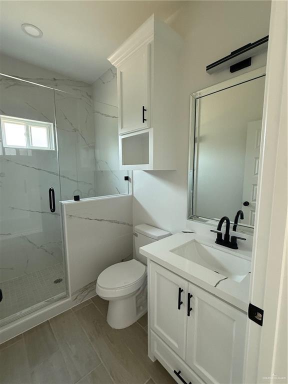bathroom featuring toilet, a marble finish shower, and vanity