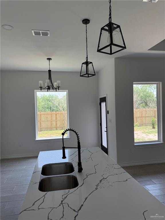 kitchen with light stone countertops, a sink, baseboards, visible vents, and pendant lighting