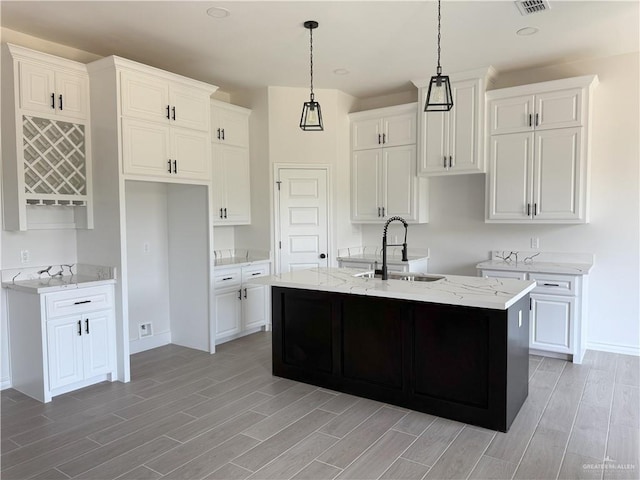 kitchen featuring light wood-style floors, a sink, an island with sink, and white cabinets