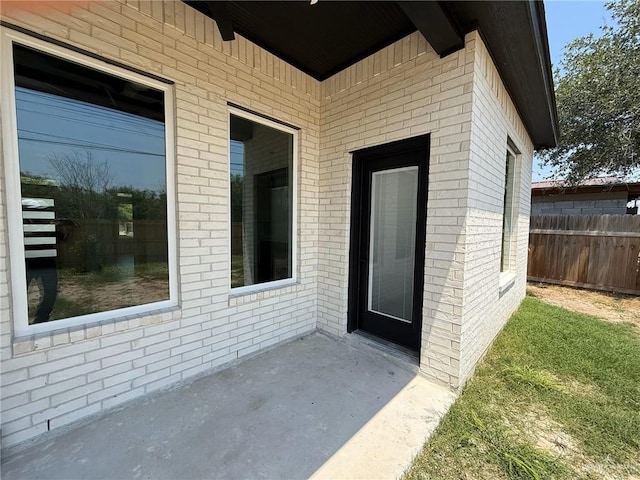 view of exterior entry featuring a patio, fence, and brick siding