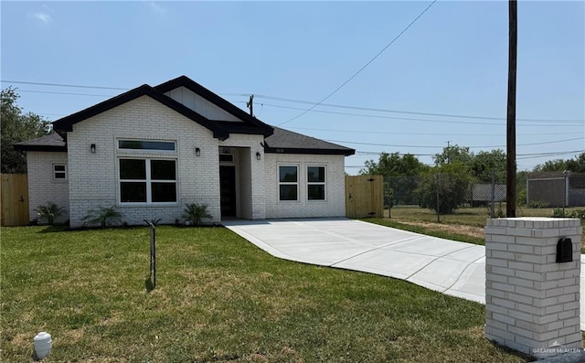 view of front of property with brick siding, a front lawn, fence, and driveway