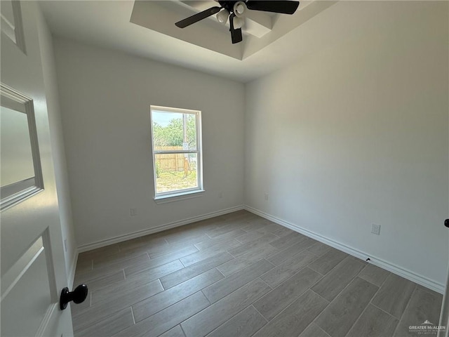 unfurnished room with a tray ceiling, wood tiled floor, baseboards, and a ceiling fan