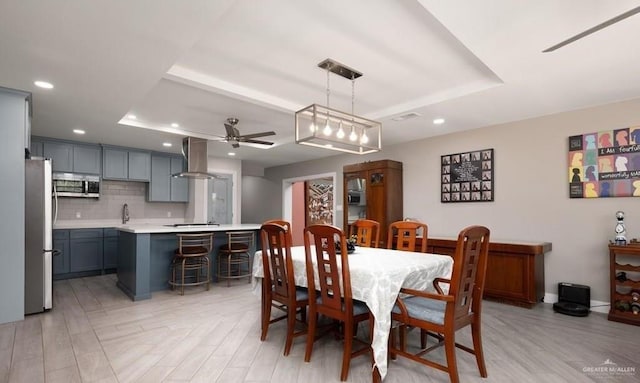 dining room featuring ceiling fan, light hardwood / wood-style floors, and a raised ceiling