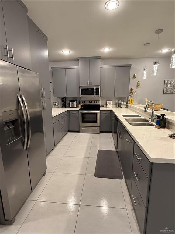 kitchen with gray cabinetry, stainless steel appliances, a peninsula, a sink, and hanging light fixtures