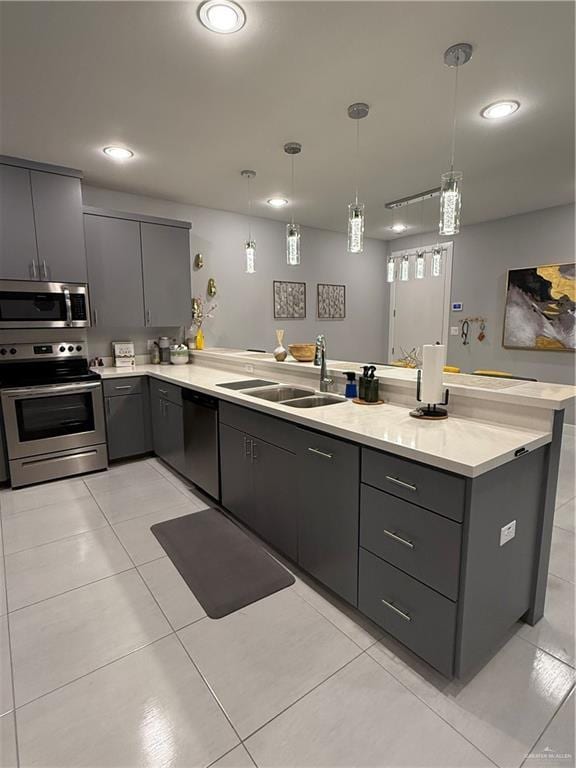 kitchen featuring stainless steel appliances, a sink, hanging light fixtures, and gray cabinetry