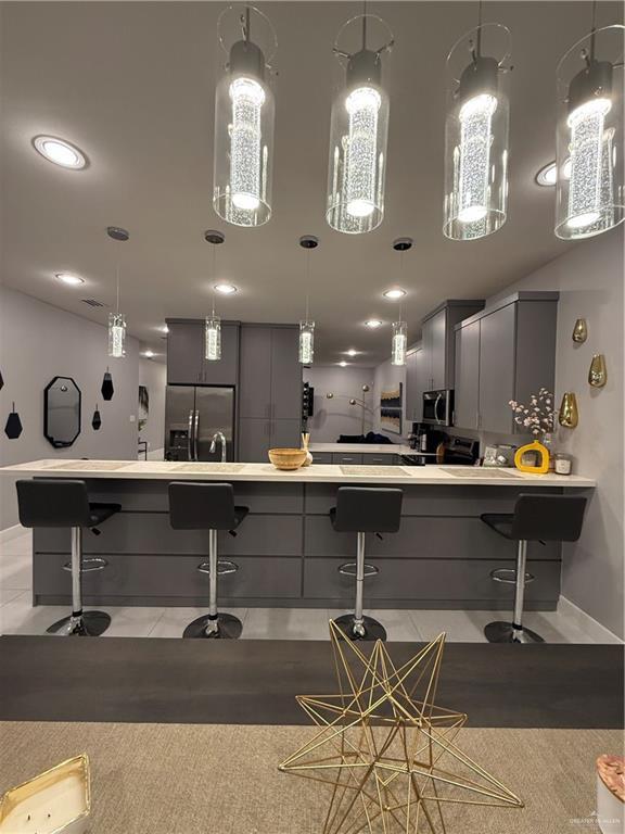 interior space featuring stainless steel appliances, a breakfast bar, light countertops, and gray cabinetry