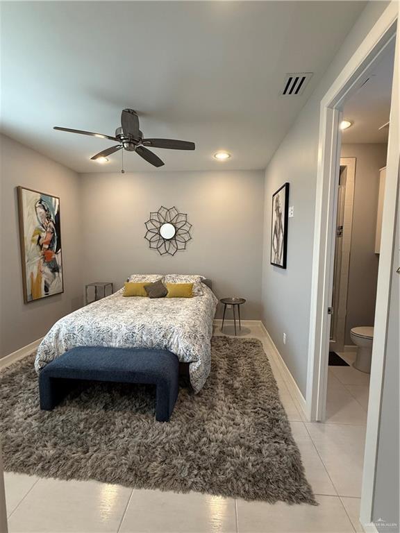 bedroom featuring ensuite bathroom, light tile patterned flooring, visible vents, a ceiling fan, and baseboards