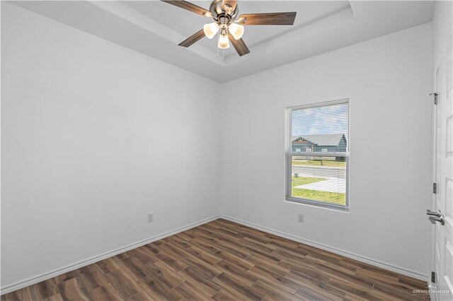 unfurnished room with a tray ceiling, ceiling fan, and dark wood-type flooring