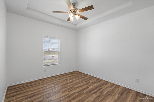 spare room with a tray ceiling, ceiling fan, and dark hardwood / wood-style floors