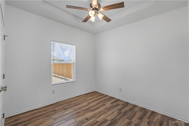 spare room with dark hardwood / wood-style flooring, a tray ceiling, and ceiling fan