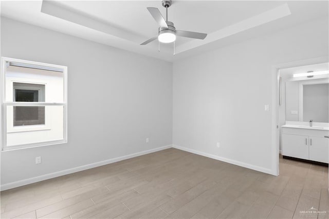 unfurnished bedroom with ceiling fan, sink, light hardwood / wood-style floors, and a tray ceiling