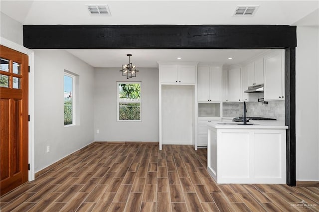 kitchen featuring decorative backsplash, stainless steel gas stovetop, white cabinets, a chandelier, and hanging light fixtures