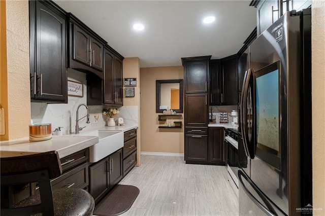 kitchen featuring stove, sink, dark brown cabinets, and stainless steel fridge