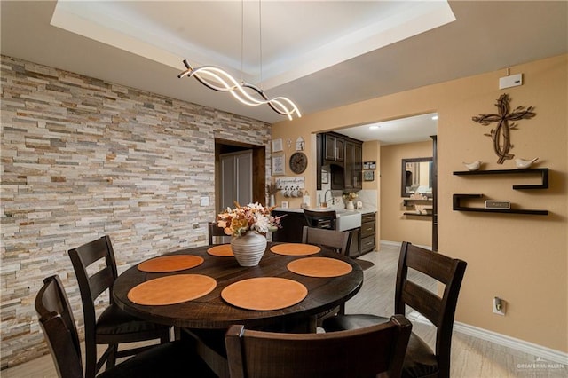 dining area featuring sink, a tray ceiling, and light hardwood / wood-style floors