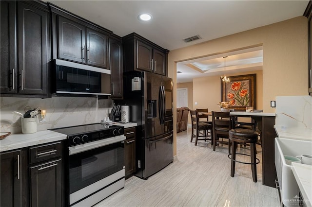 kitchen with tasteful backsplash, decorative light fixtures, black refrigerator with ice dispenser, a raised ceiling, and range with electric cooktop