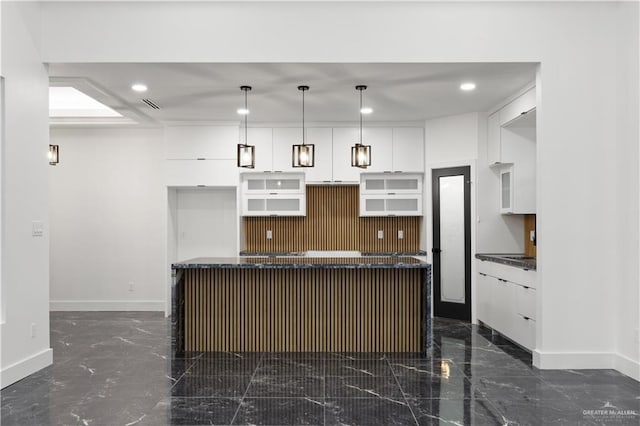 kitchen with tasteful backsplash, a kitchen island with sink, white cabinets, and pendant lighting