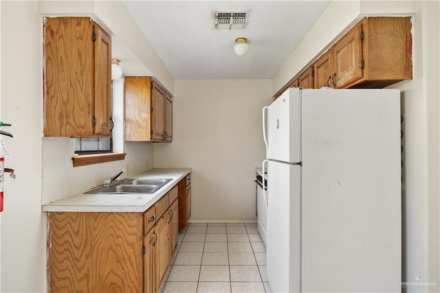 kitchen with light tile patterned floors, a sink, visible vents, light countertops, and freestanding refrigerator