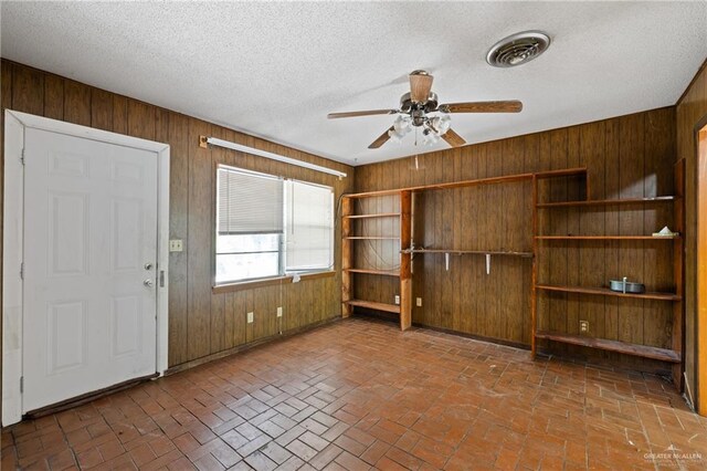 1215 Oak St, Mission, TX 78572 - unfurnished living room featuring wood walls, ceiling fan, brick flooring, and a textured ceiling