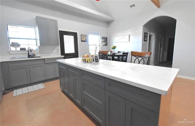 kitchen with lofted ceiling, sink, gray cabinets, light stone countertops, and a kitchen island