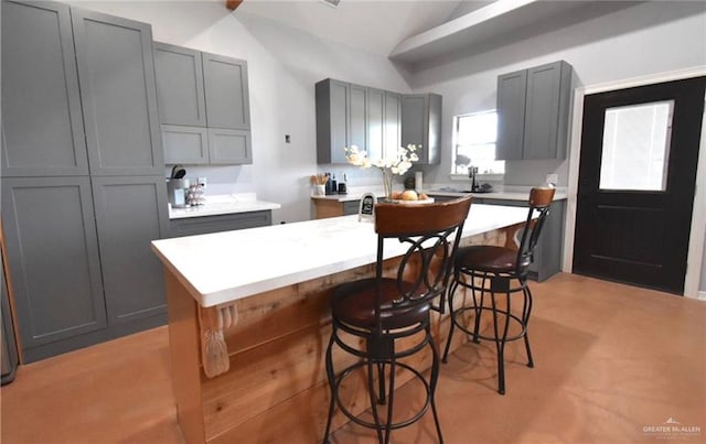 kitchen with gray cabinets, a breakfast bar, an island with sink, and vaulted ceiling