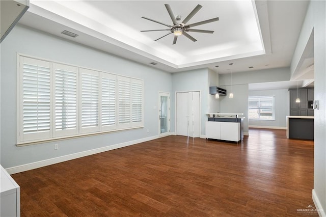 unfurnished living room with ceiling fan, dark hardwood / wood-style flooring, a wall unit AC, and a tray ceiling