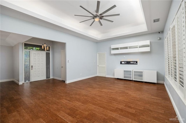 unfurnished living room with a raised ceiling, ceiling fan with notable chandelier, and dark hardwood / wood-style floors