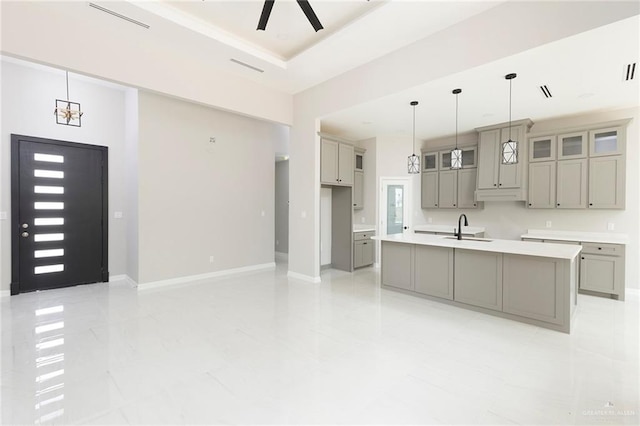 kitchen featuring gray cabinetry, ceiling fan, sink, decorative light fixtures, and a kitchen island with sink