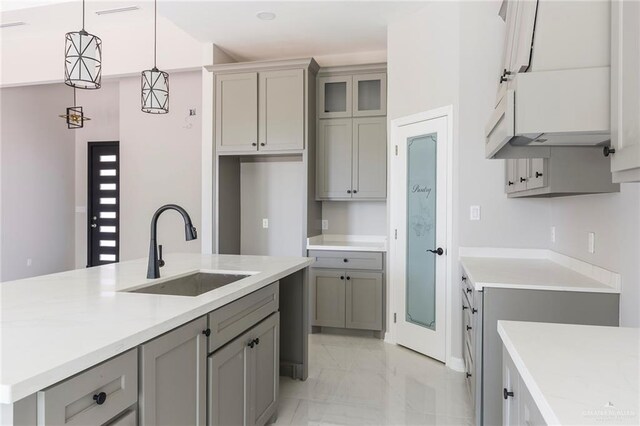 kitchen featuring gray cabinets, sink, decorative light fixtures, and a center island with sink