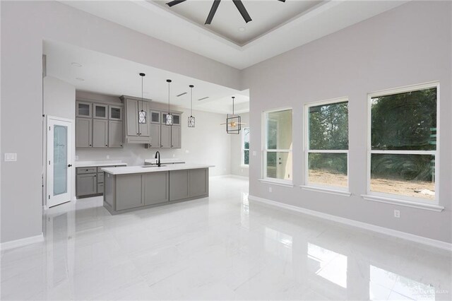 kitchen featuring pendant lighting, a center island with sink, sink, ceiling fan, and gray cabinets