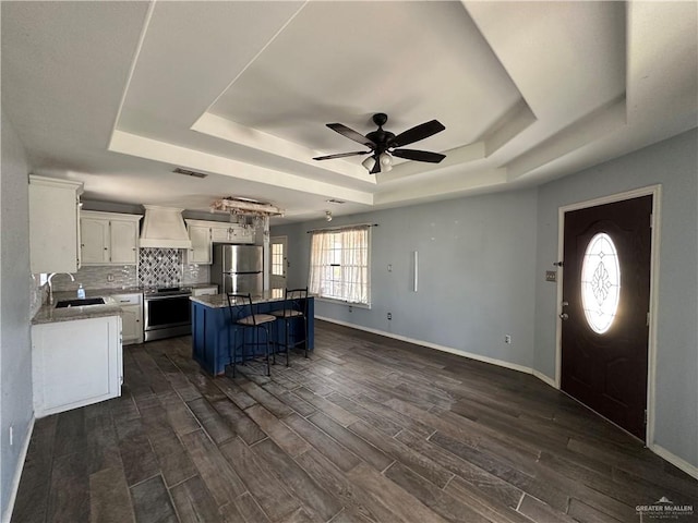 kitchen with a center island, stainless steel appliances, a tray ceiling, a breakfast bar area, and white cabinets