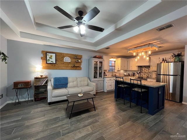 living room featuring a tray ceiling, ceiling fan, sink, and dark hardwood / wood-style floors