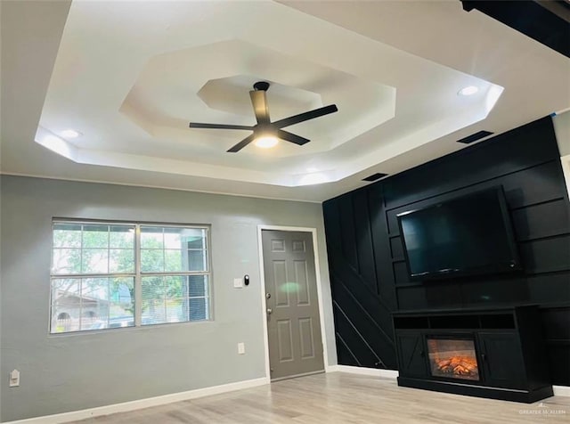foyer entrance with a fireplace, light hardwood / wood-style flooring, a raised ceiling, and ceiling fan
