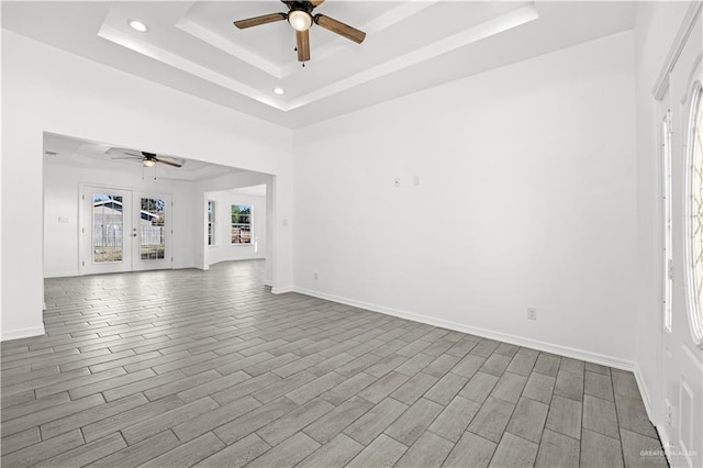 unfurnished living room featuring a raised ceiling, french doors, light hardwood / wood-style flooring, and ceiling fan