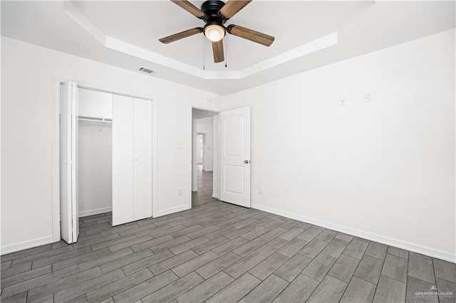 unfurnished bedroom featuring ceiling fan, a raised ceiling, dark wood-type flooring, and a closet