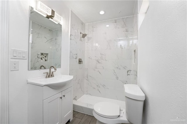 bathroom featuring a tile shower, hardwood / wood-style floors, vanity, and toilet